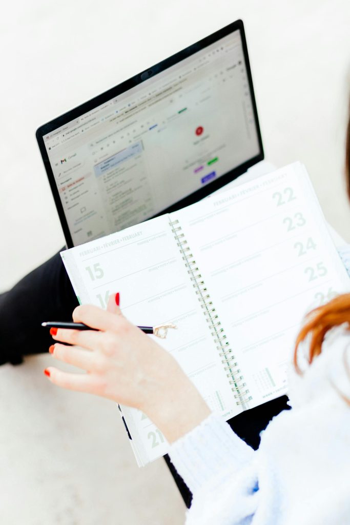 Woman using laptop and notebook for work organization and schedule planning indoors.